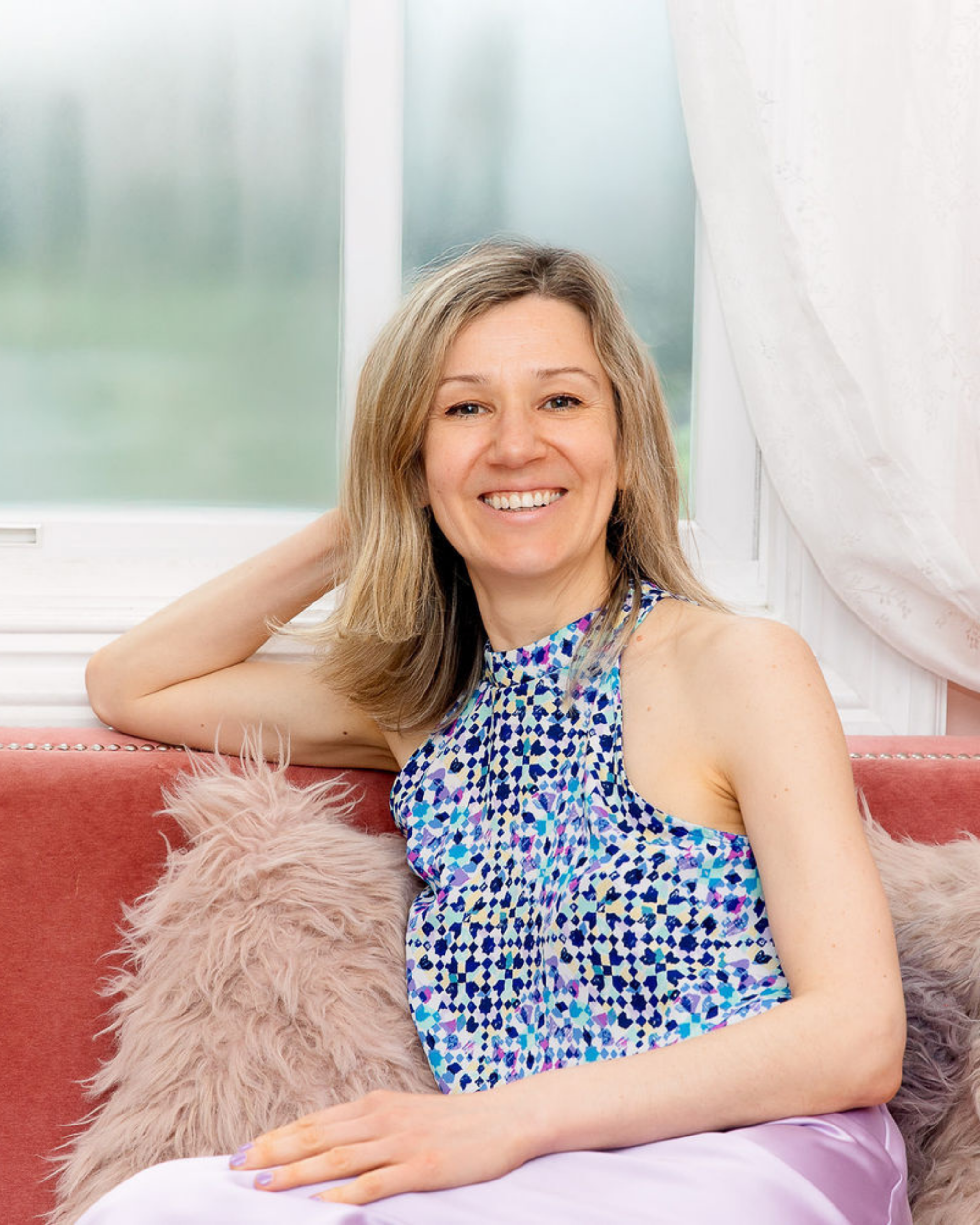 Dasha smiling on a couch in a blue patterned top.